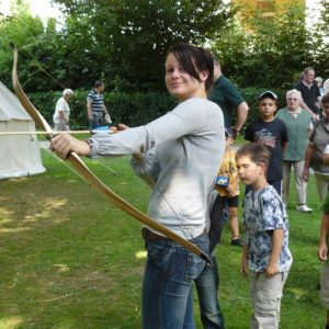 Foto junge Frau beim Bogen schießen auf einer Wiese mit anderen Besuchern