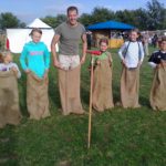 Sack hüpfen auf einem mittelalterlichen Fest, auf einer grünen Wiese im Sommer, ein Mann und 5 Kinder